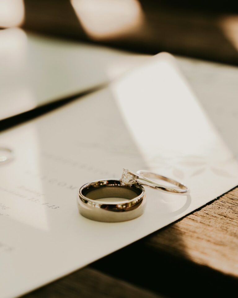 A couple holds hands and looks at an open notebook while sitting at a table with coffee and wedding magazines.