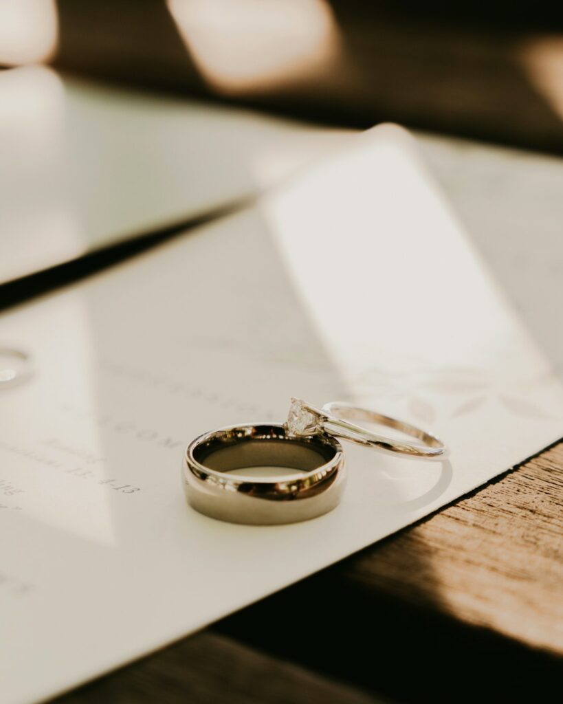 A couple holds hands and looks at an open notebook while sitting at a table with coffee and wedding magazines.