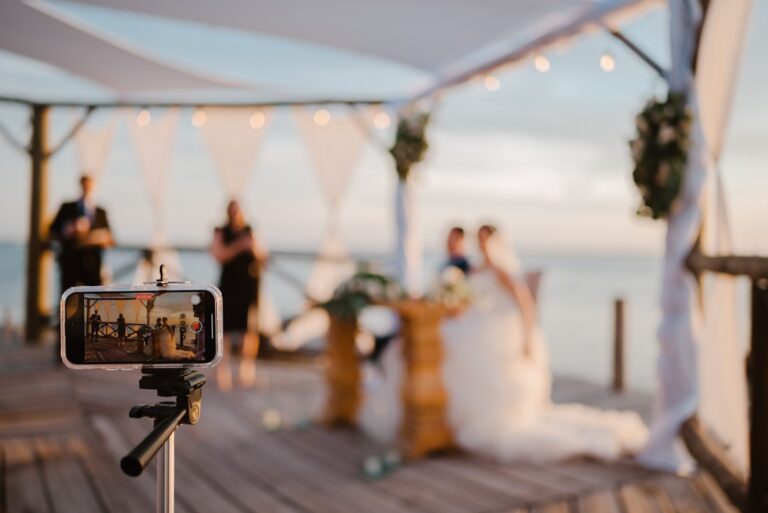 A wedding ceremony with guests seated outdoors and a camera set up for livestreaming.