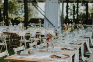 Guests share a seasonal wedding dinner at long tables beside an outdoor reception setup.